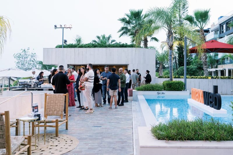 Guests mingling on a paved pool terrace beside orange and black maxweb letters in the water