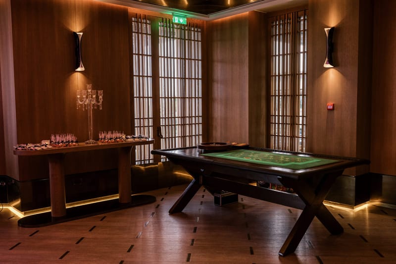 Roulette table in a wood-panelled room beside a side table of favors under a crystal candelabra