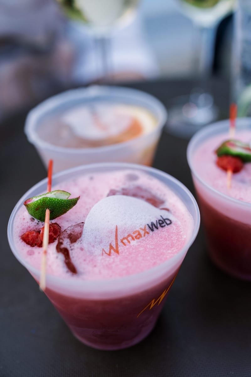 Pink cocktails with lime and strawberry garnishes in clear cups printed with the maxweb logo