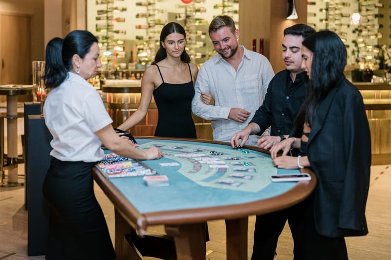 Dealer at a blackjack table as four guests place chips and laugh together