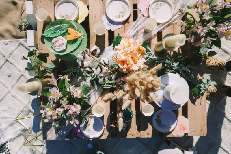 Overhead view of a pallet table with floral paper plates, cups, candles and peach and lilac flowers