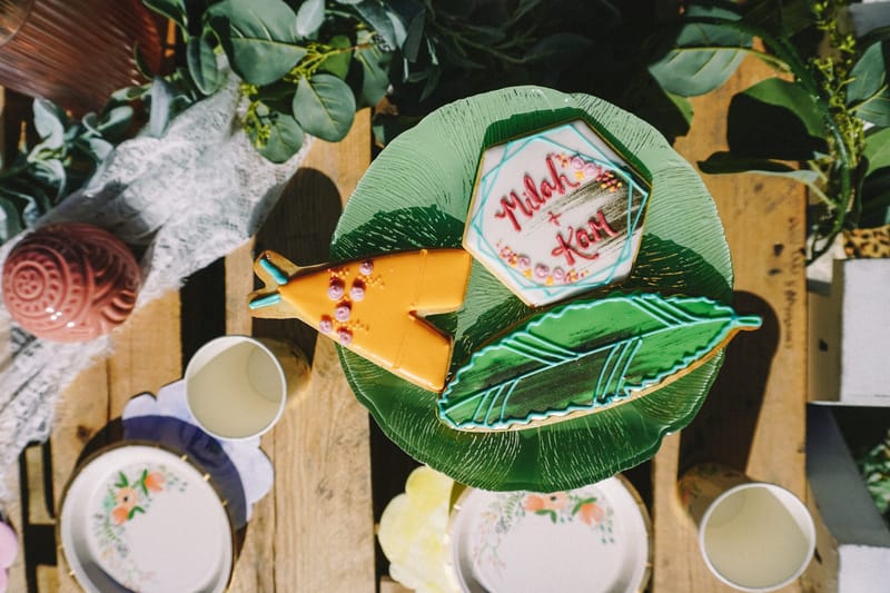 Iced cookies on a green glass plate, one reading Milah + Kam beside a leaf-shaped cookie