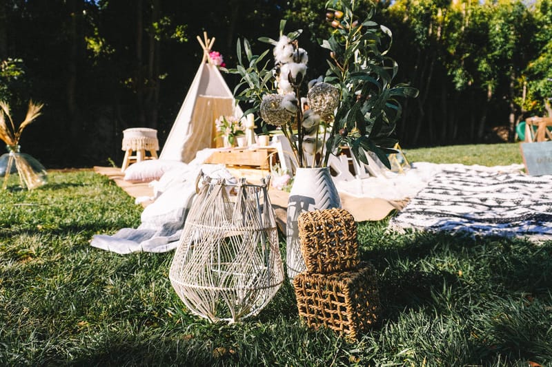 White wire lantern and woven basket cubes on the lawn in front of a teepee and picnic blankets