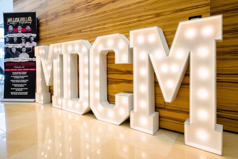 Giant lit MDCM marquee letters beside a Million Dollar Credit Mastermind speaker banner