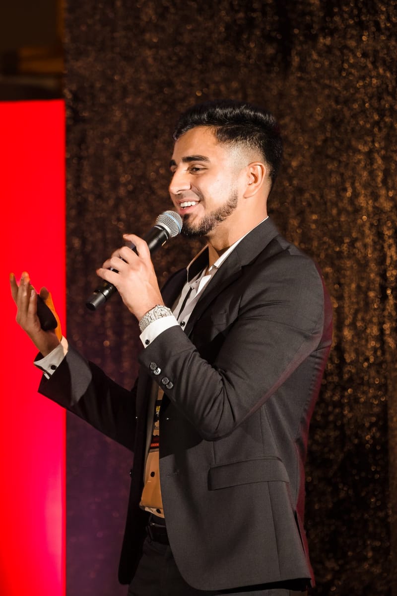 Smiling speaker with a microphone in front of red and dark sequin panels