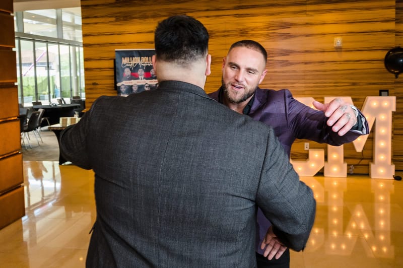 Two men greeting each other in front of lit MDCM letters and a wood-paneled wall