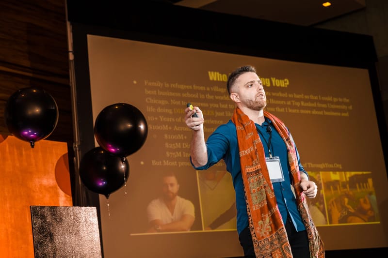 Speaker in an orange paisley scarf presenting a text slide beside black balloons