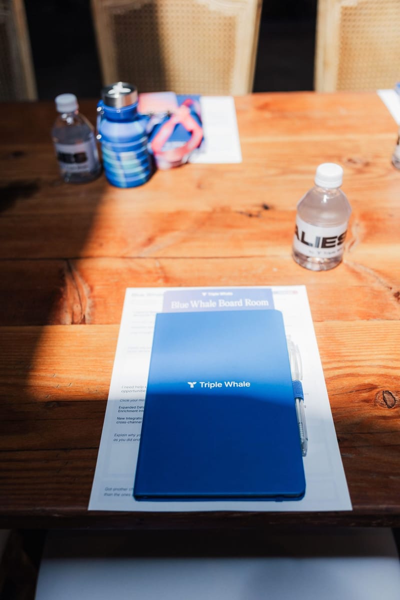 Blue Triple Whale notebook and pen on a printed Blue Whale Board Room sheet on a wooden table