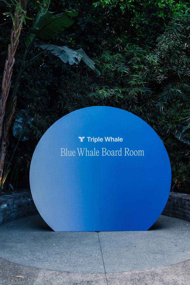 Round blue sign reading Triple Whale Blue Whale Board Room in front of greenery