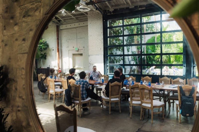 Tables of guests reflected in a round mirror, with glass garage doors behind