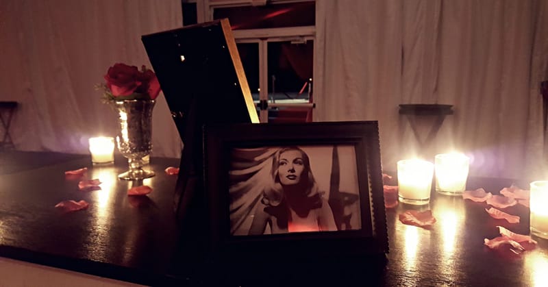 Framed black and white portrait of a woman with long wavy hair beside a rose, candles and scattered petals