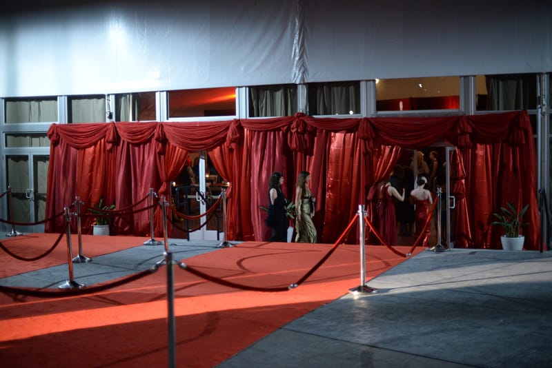 Red carpet lined with posts and red ropes leading to a tent entrance draped in red curtains