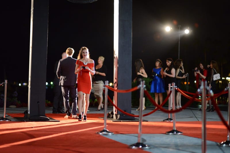 Guests posing on the red carpet between posts and red ropes at night