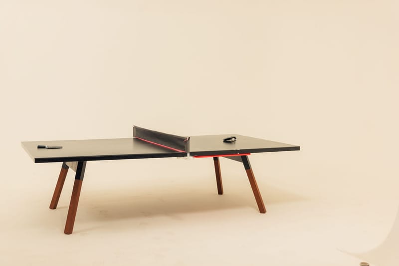 Black ping pong table with wooden legs against a cream backdrop