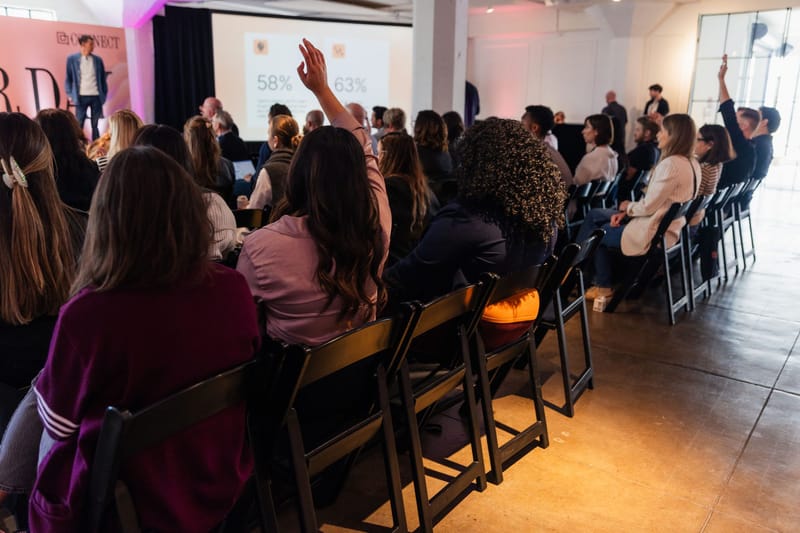 Audience raising hands during a talk, with a slide showing 58% and 63%