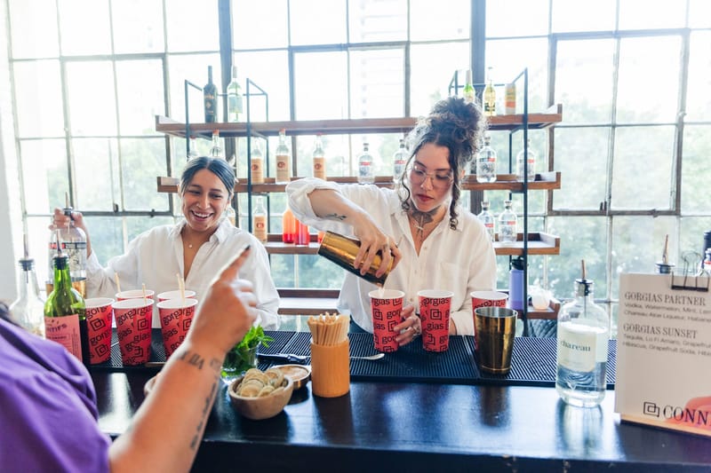 Two bartenders pouring into red Gorgias cups beside a menu listing the Gorgias Partner and Gorgias Sunset