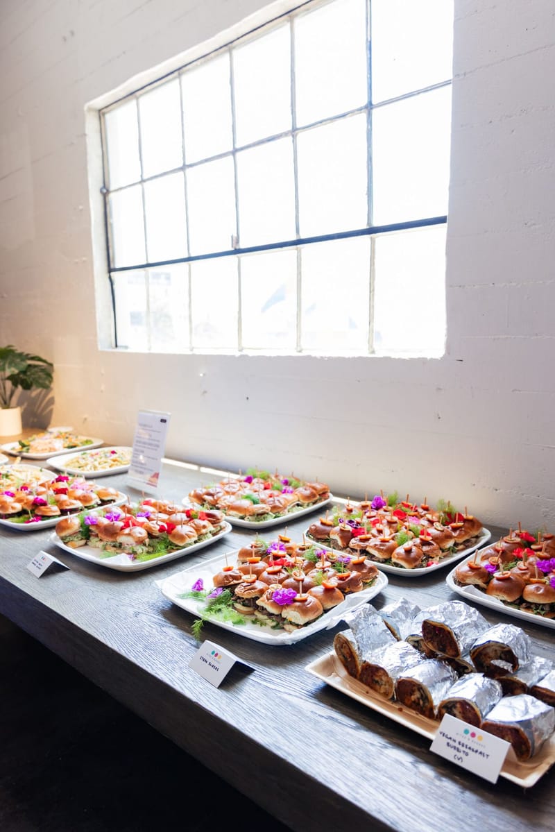 Platters of sliders with edible flowers beside cards reading Steak Sliders and Vegan Breakfast Burrito