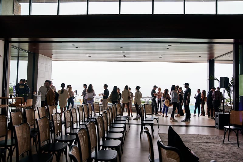 Guests gathered at an open glass wall behind rows of empty chairs in a high-ceilinged room