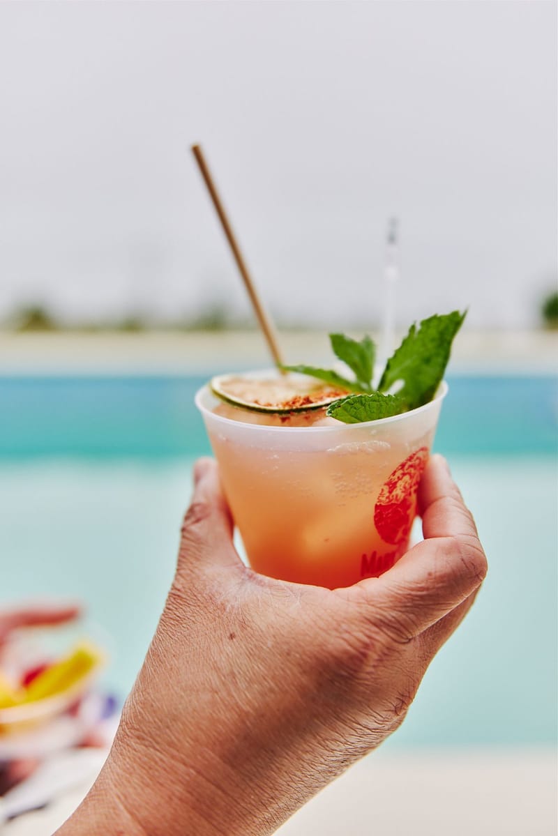 Hand holding an iced drink with mint and a dried citrus slice above a blue pool