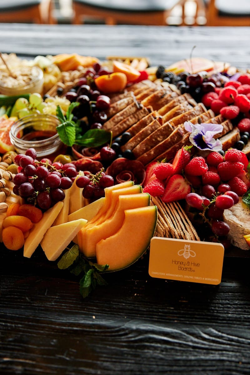 Grazing board of melon, strawberries, cherries and bread with an orange Honey & Hive Boards card