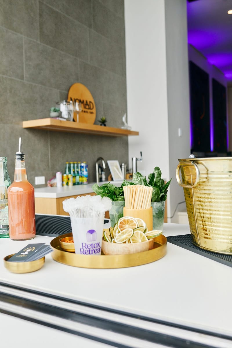 Bar counter with a Retox Retreat cup of stirrers, straws, dried limes, fresh herbs and a gold ice bucket