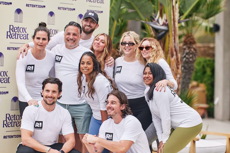 Group of guests in matching white shirts posing in front of a Retox Retreat and Retention logo backdrop