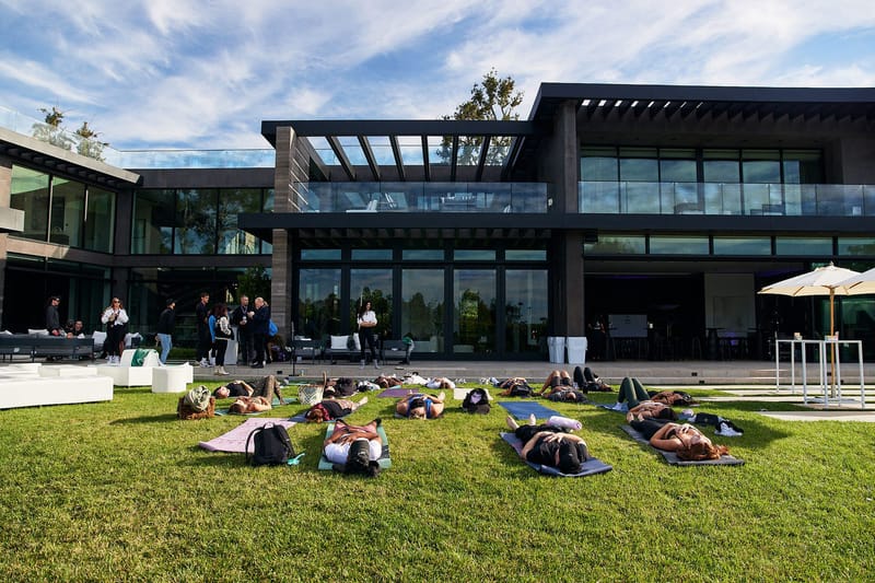 Guests doing yoga on mats across the lawn in front of a modern glass house
