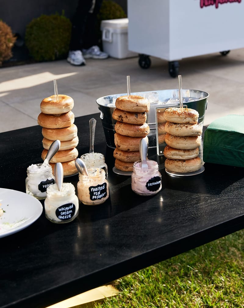 Bagels stacked on stands beside jars of cream cheese spreads with chalkboard labels