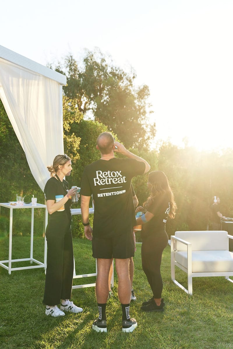 Guests in black Retox Retreat and Retention shirts talking on the lawn in late sun