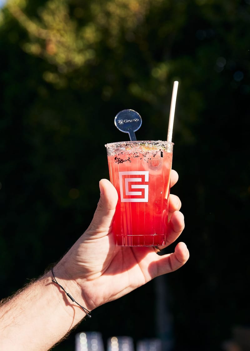 A hand holding a red drink with a crusted rim and a round branded stirrer