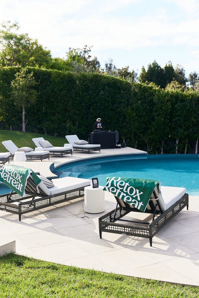 Poolside loungers draped with green Retox Retreat towels, with the hedge lined pool beyond