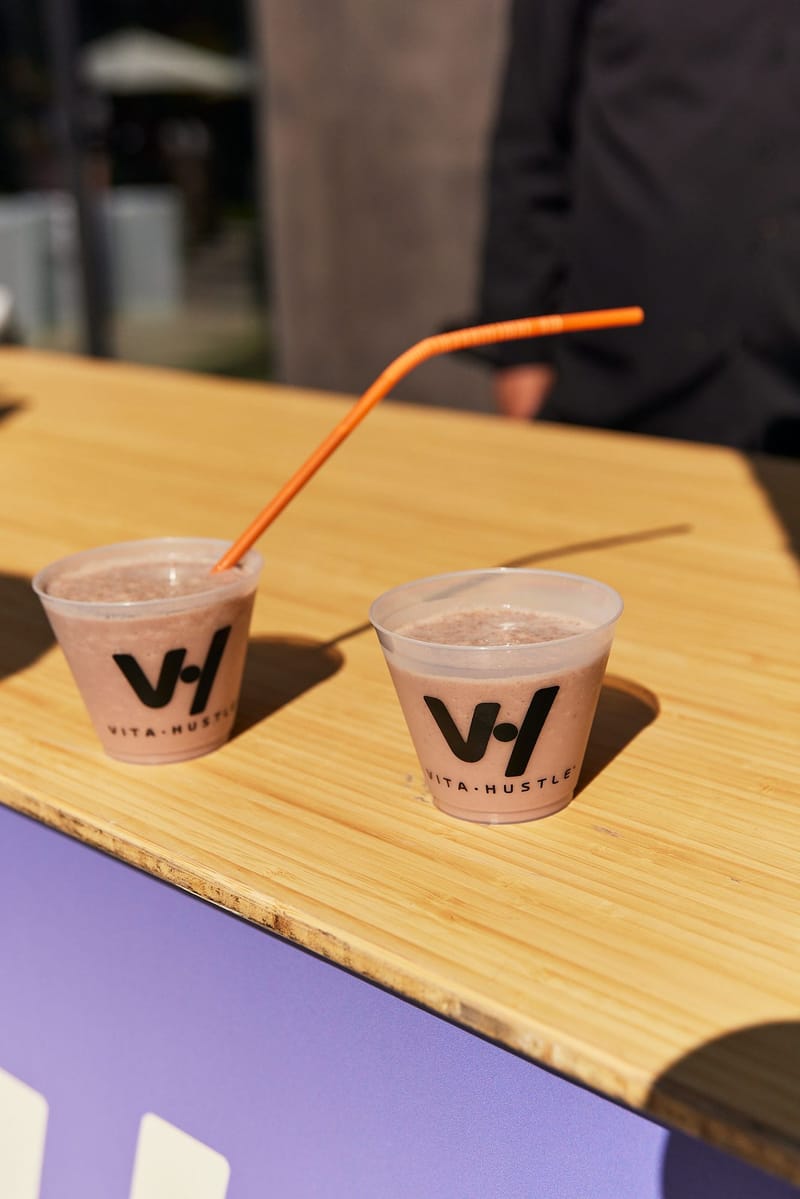 Two Vita Hustle cups of a pink drink on a wooden counter
