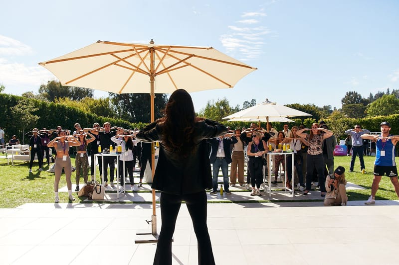 A woman under a white umbrella leading a group of guests through a movement session on the lawn