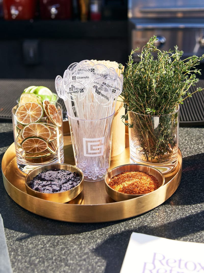 Gold tray with dried citrus, herbs, bowls of seasoning and clear branded stirrers