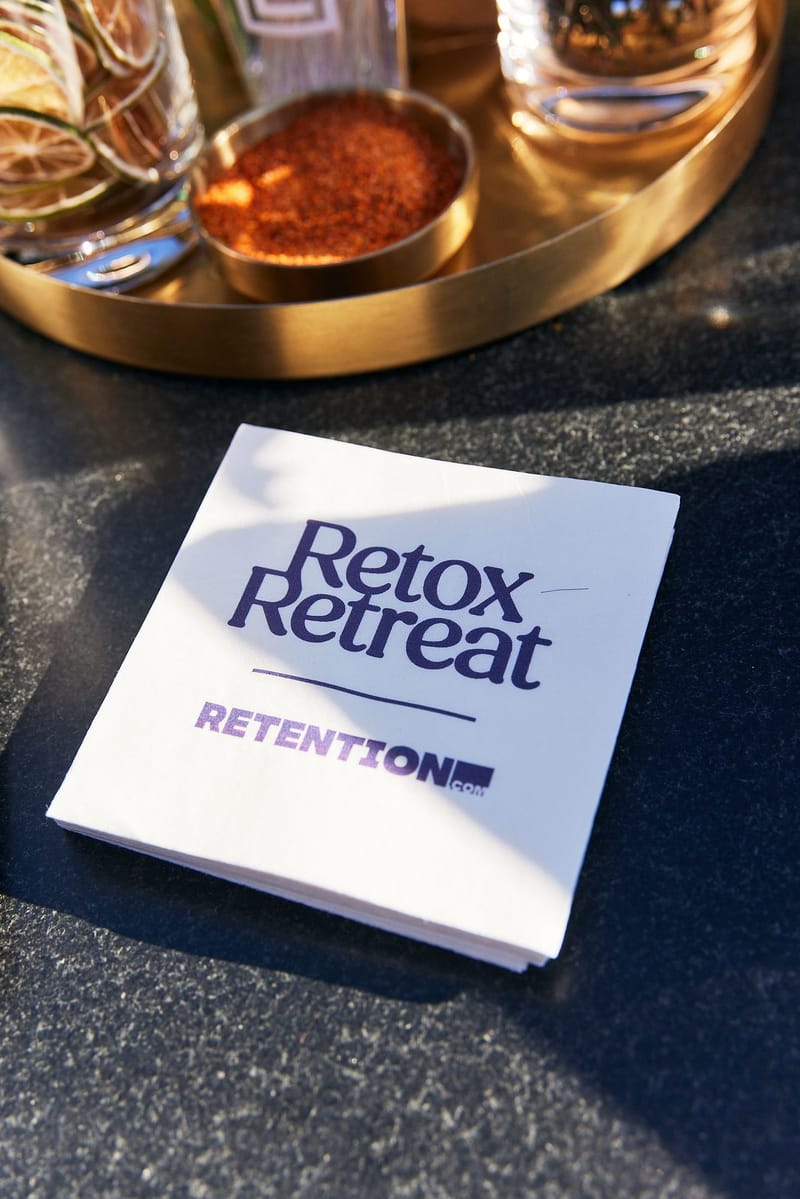White Retox Retreat and Retention napkin on a dark bar beside a gold tray
