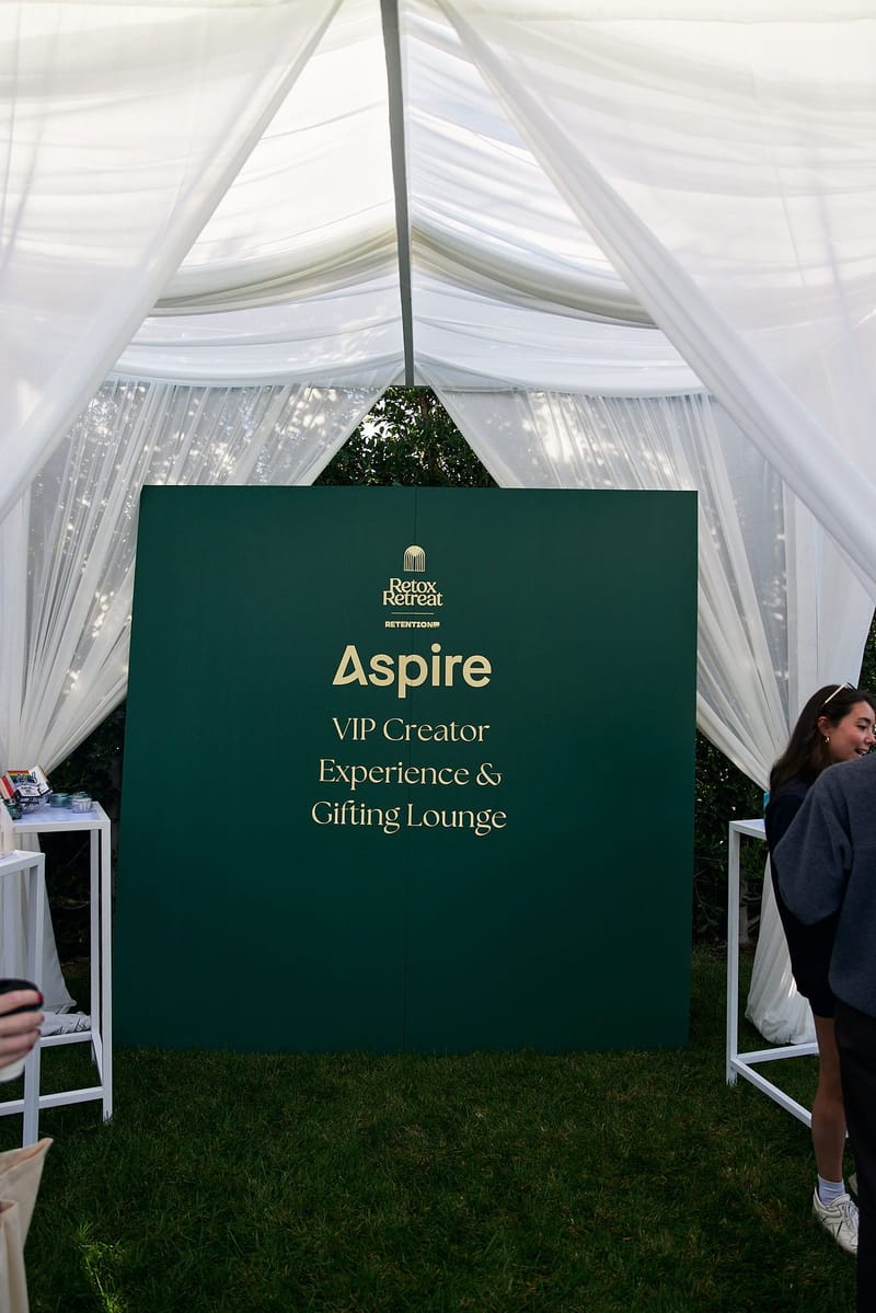 Green sign for the Aspire VIP Creator Experience & Gifting Lounge inside a white draped tent