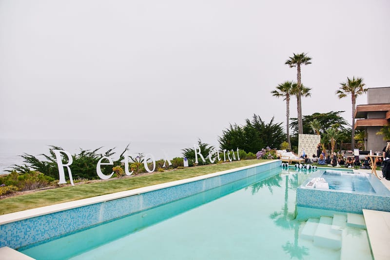 Long pool with a blue mosaic edge below large white Retox Retreat letters along the lawn
