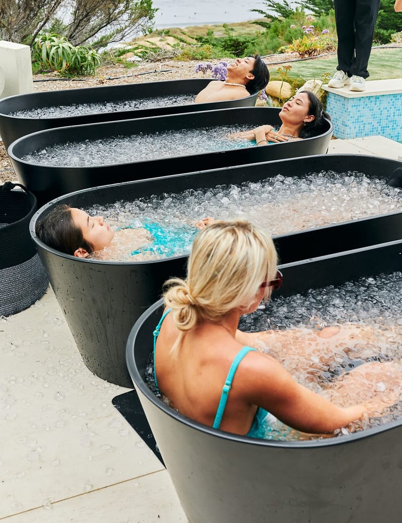 Four guests leaning back in black ice bath tubs filled with crushed ice