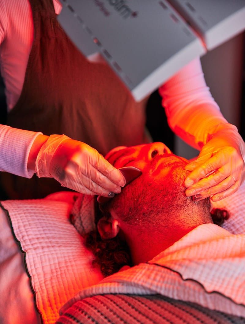 Gloved practitioner giving a guest a facial with a gua sha stone under red light