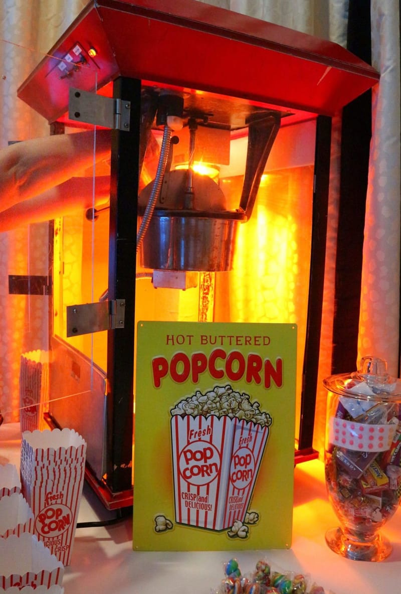 Popcorn machine behind a yellow Hot Buttered Popcorn sign, with striped popcorn boxes and a glass jar of candy