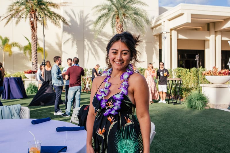 Guest in a purple flower lei smiling on the lawn beside a table with blue napkins