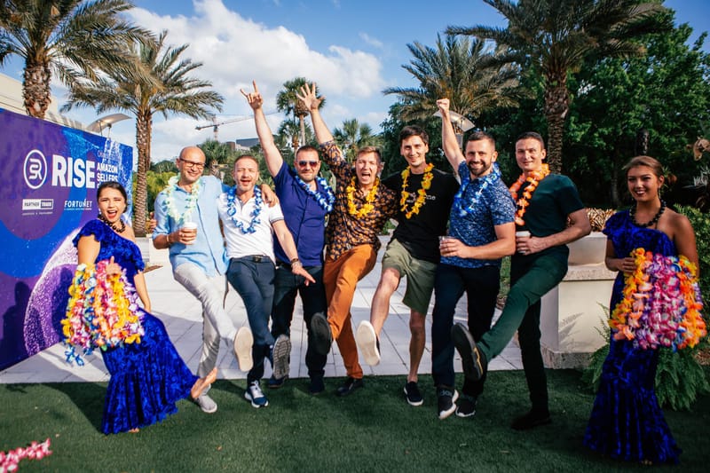 Performers in blue dresses and guests kicking up their legs in front of a RISE Amazon Sellers backdrop with a planet graphic