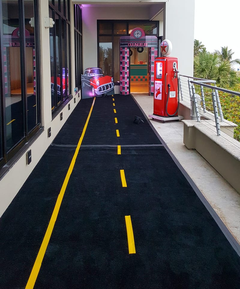 Black carpet with yellow road lines leading to a DINER doorway, a red car cutout and a red Texaco pump