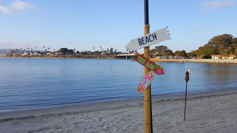 Bamboo post with arrow signs reading BEACH and TIKI BAR and a pink surfboard sign reading TIKI TIME!