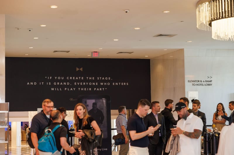 Attendees talking in a bright foyer beneath a chandelier and a black wall printed with a quote