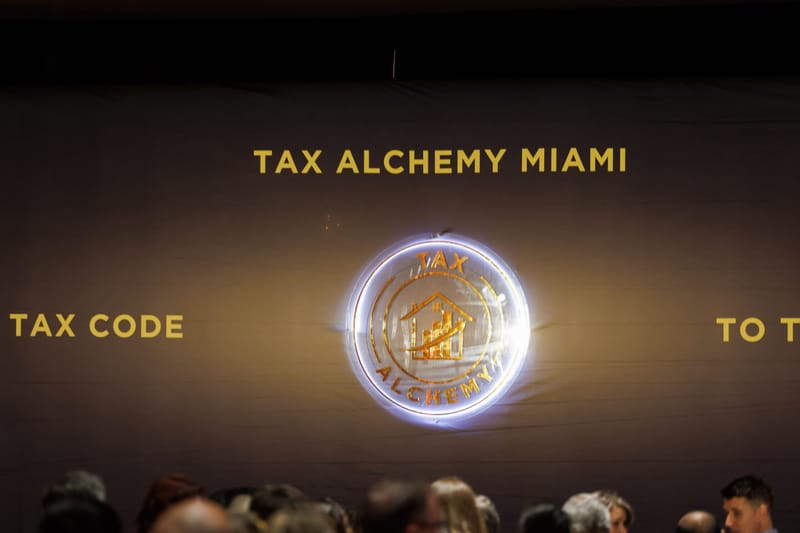 Glowing round Tax Alchemy logo on a backdrop printed with Tax Alchemy Miami