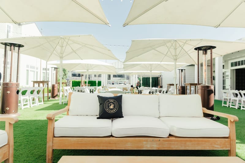 White outdoor sofa with a black Tax Alchemy pillow under large white umbrellas