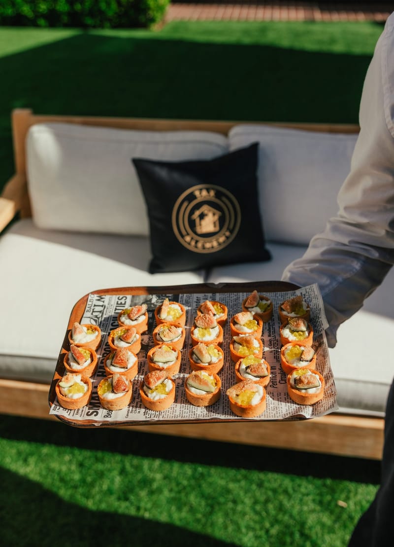 A server holding a tray of small bites beside a sofa with a Tax Alchemy pillow