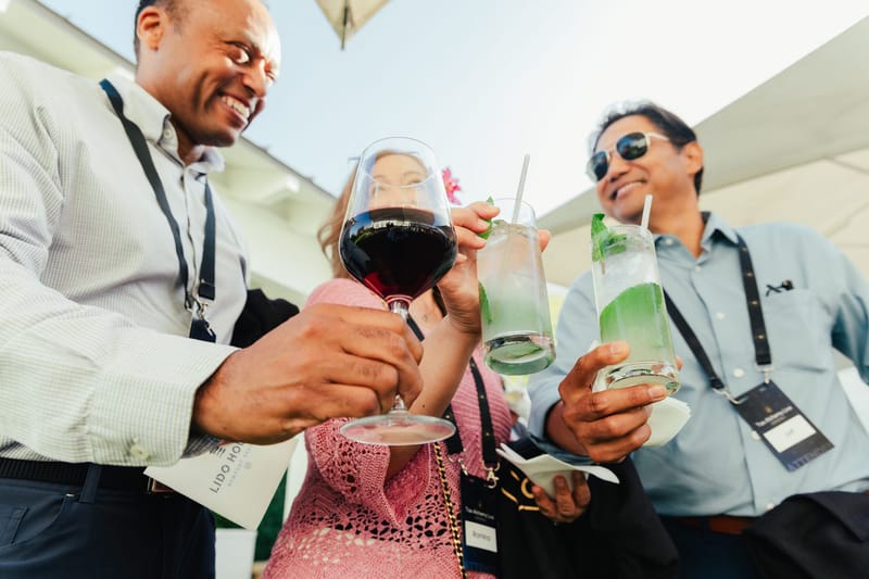 Three guests wearing lanyards raising a glass of red wine and two green cocktails