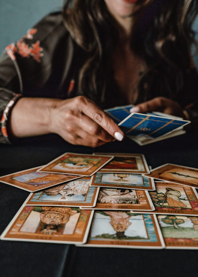 Hands dealing illustrated tarot cards across a black tablecloth